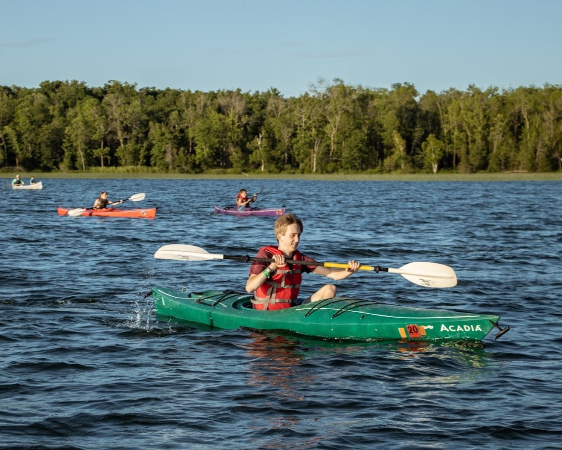 A Scout is kayaking in the lake. Two other kayaks are visible in the background.