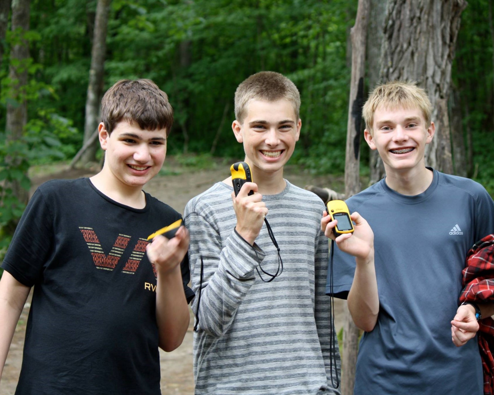 Three Scouts are smiling and showing off a GPS device