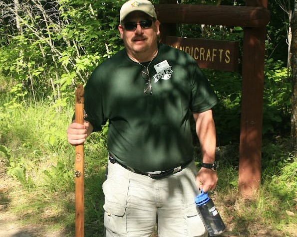 An adult leader wearing sunglasses holding a hiking staff with a water bottle clipped to his their waist