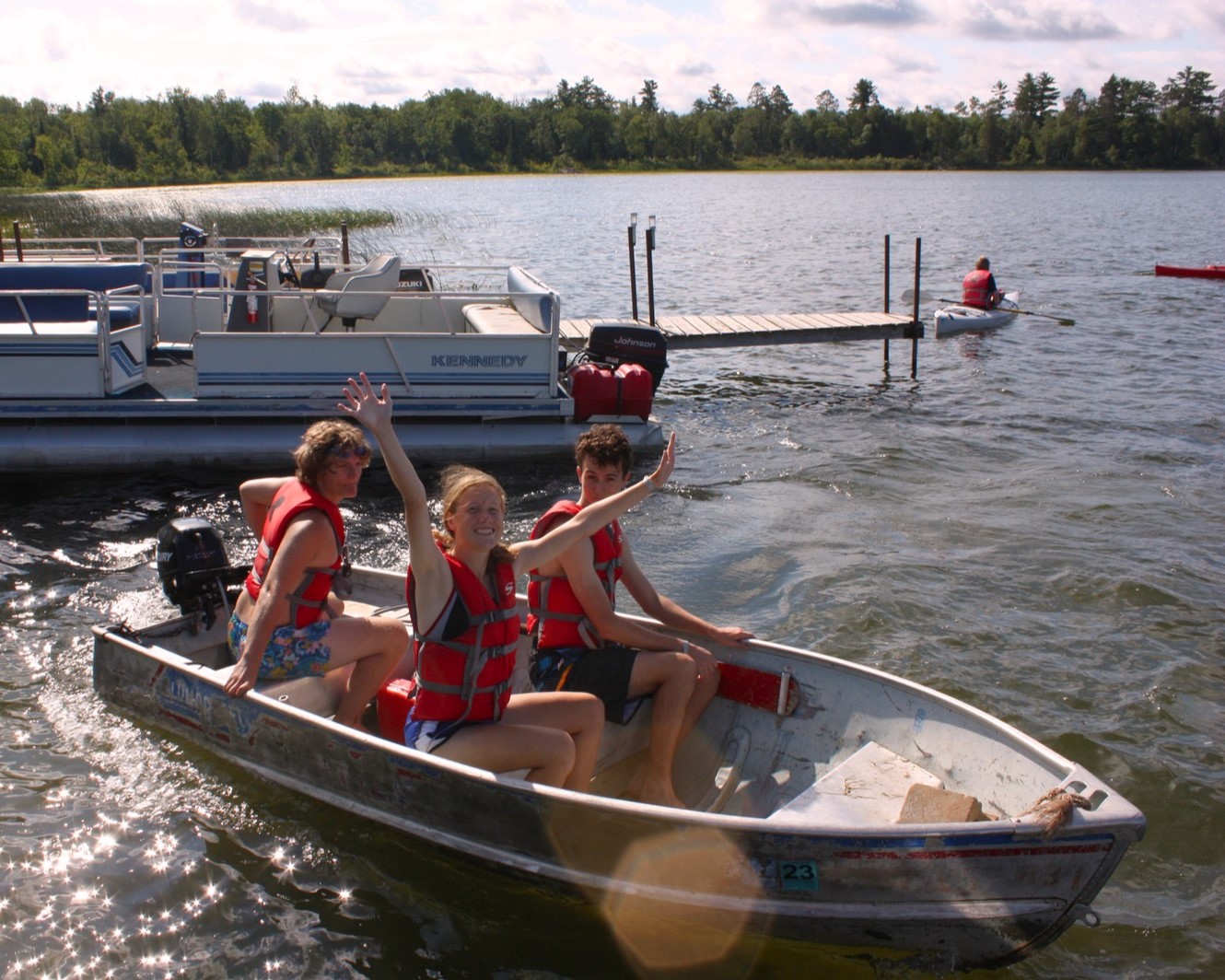 A staff member and two smiling Scouts are taking off in a motor boat